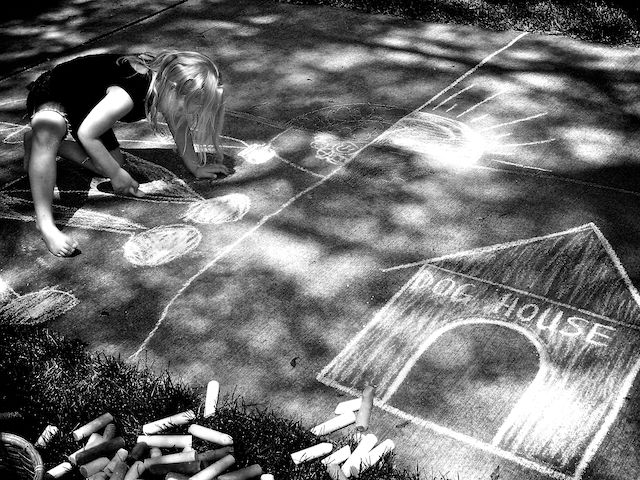 dog house and sun drawn on the sidewalk with chalk, girl drawing nearby