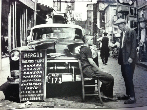 (old picture of 2 men and a taxi in the street)